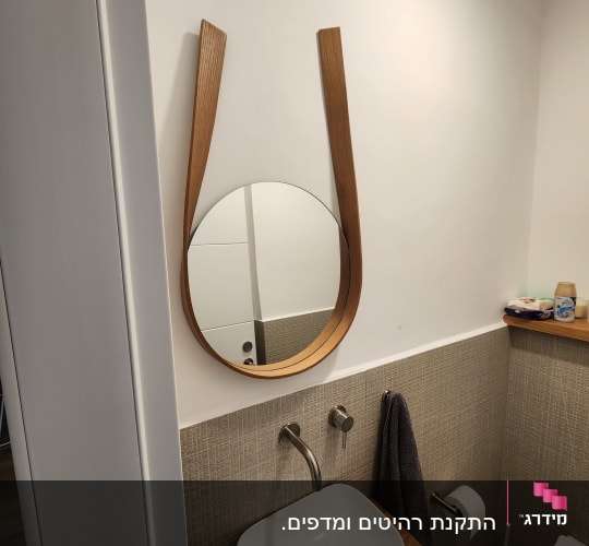 כיור עם ברז ומראה עגולה בחדר אמבטיה